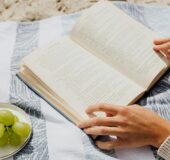Person reading a book with grapes and her sunglasses on the beach