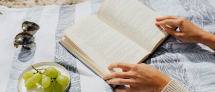 Person reading a book with grapes and her sunglasses on the beach