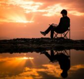 Someone in a chair reading a book as the sun sets